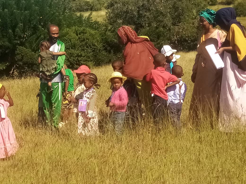 Un groupe d'enfants et d'enseignants marche à travers un champ d'herbes hautes à Dzahadjou