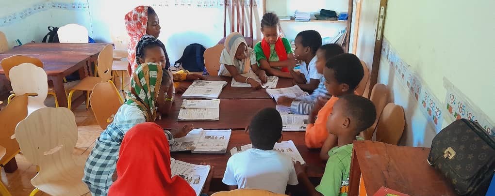 Des élèves de la Maison des Enfants Lumières installés autour de tables regroupées, travaillant sur des livres et des cahiers dans leur classe